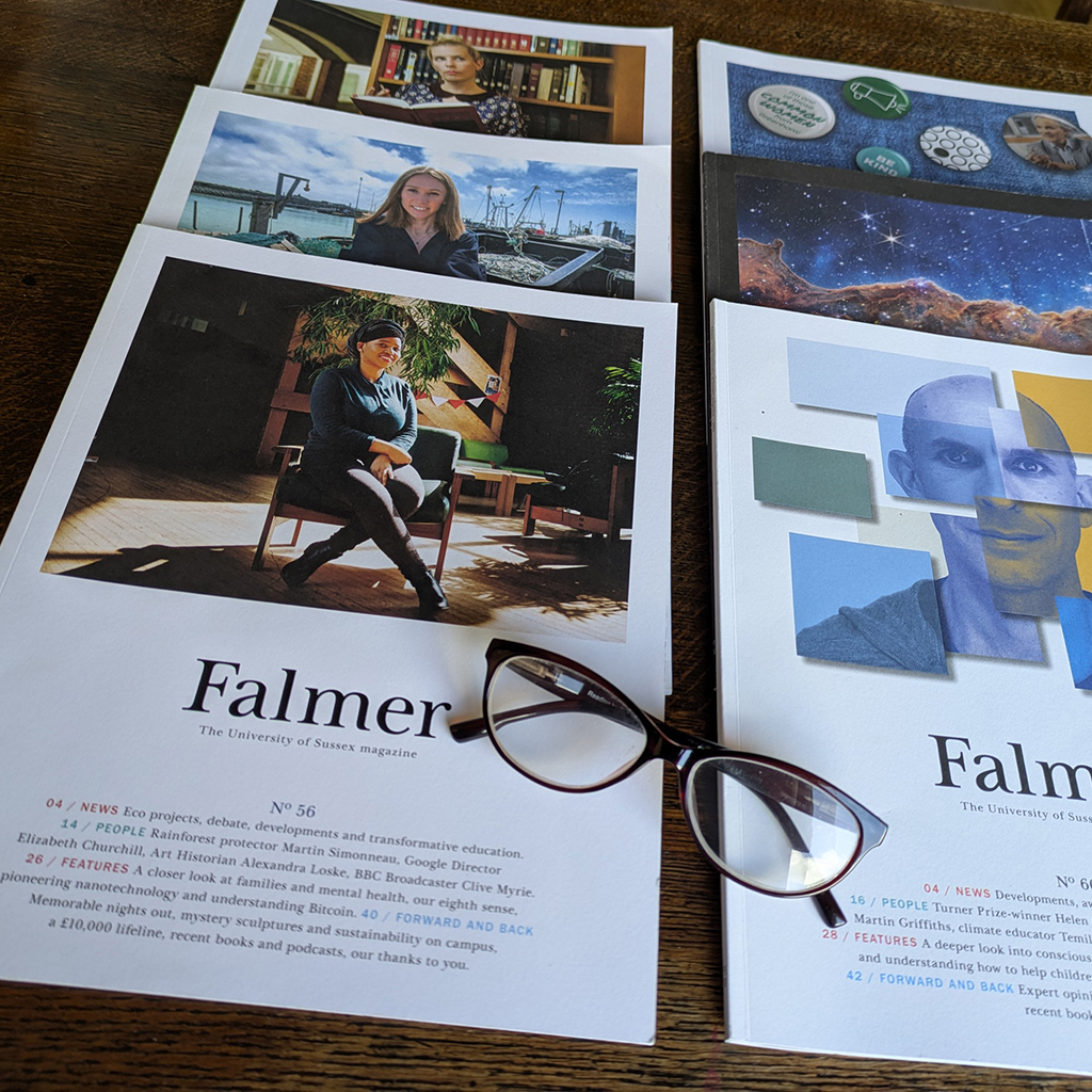 Six different printed editions of Falmer magazine on a table with reading glasses